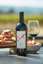 Photo of a bottle of 2020 HALL Craig's Cabernet Sauvignon on a picnic table with a platter of sandwiches, a summer salad, and glass of red wine in the background.