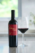 A bottle of Kathryn Hall Cabernet Sauvignon on a granite countertop next to a glass of red wine.