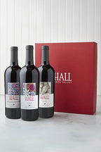 Image of the HALL Artful Giving Wine Set containing three bottles of HALL Cabernet in font of a red HALL gift box.