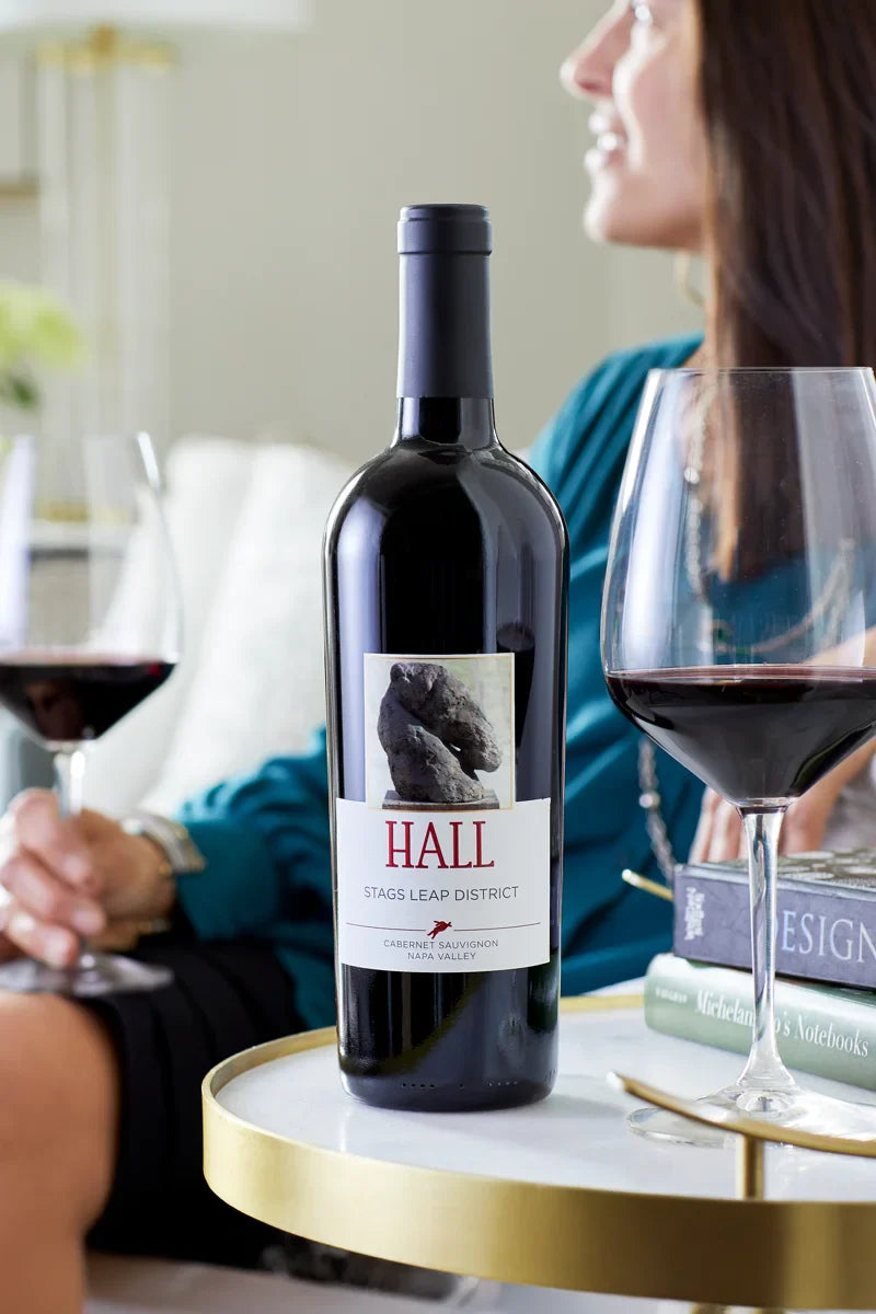 Bottle of Hall Stags Leap District Cabernet Sauvignon wine on a table with a woman sitting in the background