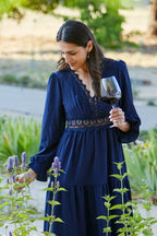 Woman wearing a blue dress admiring a garden while holding a glass of 2022 HALL Coeur Cabernet Sauvignon.